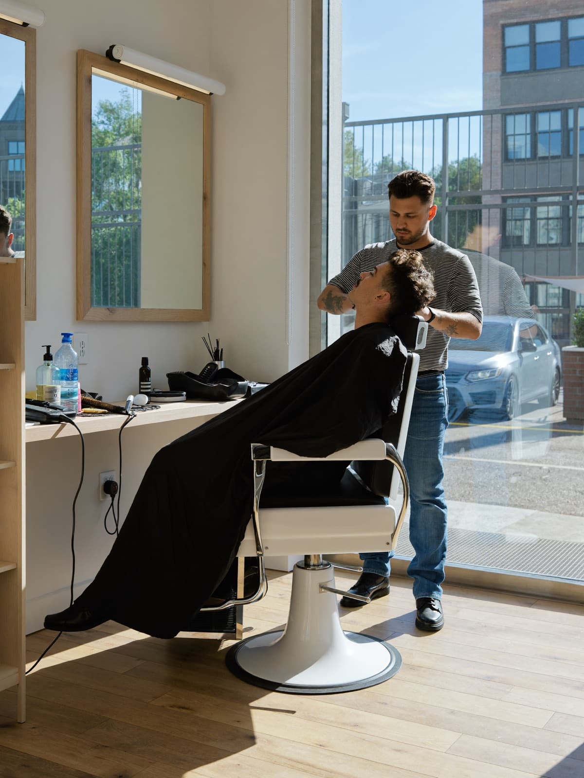 Barber giving a client a haircut by the window of a bright, modern barbershop